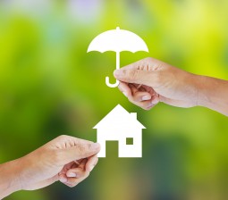 a hand holding a paper cutout of an umbrella over a cutout of a house to illustrate property management